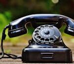Close-up of a classic black rotary phone outdoors with a blurred green background.